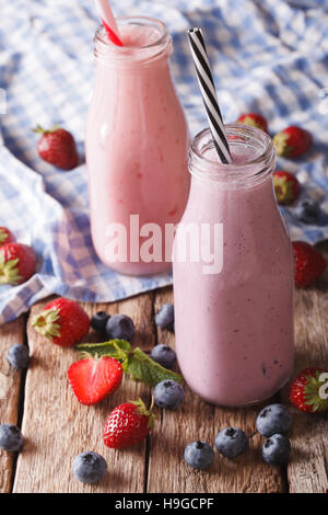 Hausgemachter Milchshake mit Erdbeeren und Heidelbeeren in Nahaufnahme der Flaschen auf den Tisch. vertikale Stockfoto