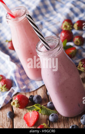 Milchshakes mit Erdbeeren und Heidelbeeren in Nahaufnahme der Flaschen auf den Tisch. vertikale Stockfoto