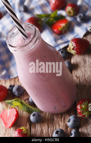 Leckere Milch Smoothie mit Erdbeeren und Heidelbeeren in Großaufnahme Glas Flasche auf dem Tisch. vertikale Stockfoto