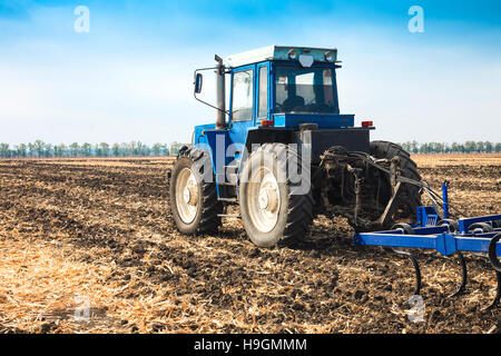 Alten blauen Traktor mit einem Pflug in einem Feld an einem sonnigen Tag. Das Konzept der Arbeit auf ein Feld und Agrarindustrie. Stockfoto