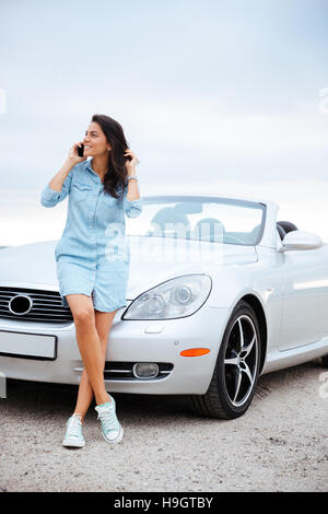 In voller Länge Portrait von einer schönen jungen Frau am Smartphone sprechen und stehen an ihrem Auto Stockfoto