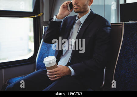 Geschäftsmann hält eine Einweg-Kaffeetasse Mobile Telefonieren während der Fahrt Stockfoto