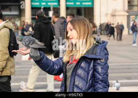 Eine junge Frau hält Lebensmittel für Tauben auf der Piazza del Duomo, Mailand, Italien Stockfoto