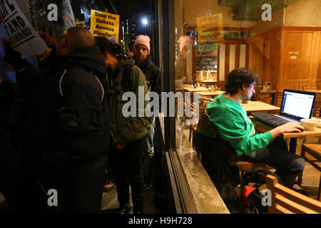 New York, USA. 23. November 2016. Eine Person, die in einem Café auf der Hand zu Aktivistinnen marschieren Außerhalb sitzt. Stockfoto