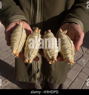 Vier torpedoförmige Spulen mit goldfarbenen Borten ruhen in den Händen eines Bortenherstellers in Fes, Marokko. Stockfoto