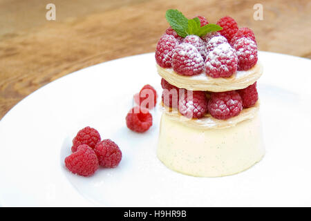 Vanille Panna Cotta mit Mille Feuille und frische Himbeeren und einem Zweig Minze, serviert auf eine große weiße Platte auf einem hölzernen Hintergrund Stockfoto