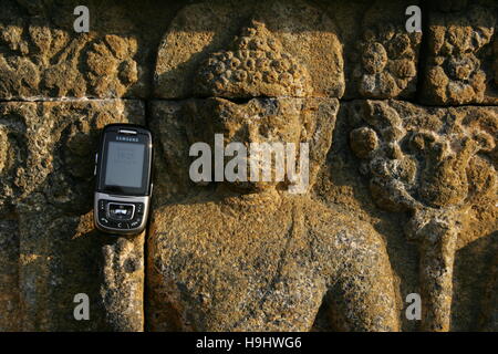 eine Erleichterung Buddah hält ein Mobiltelefon zu Borobudur in Zentraljava, Indonesien Stockfoto