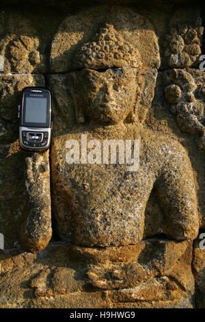 eine Erleichterung Buddah hält ein Mobiltelefon zu Borobudur in Zentraljava, Indonesien Stockfoto