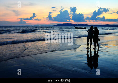 Sonnenuntergang in Aonang Beach in der Region Krabi (Thailand). Es gibt die Silhouette eines Paares, dessen Schatten und ein Boot Stockfoto