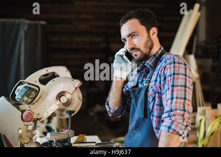 Porträt von Schreiner anrufen mit Smartphone in der Werkstatt Stockfoto