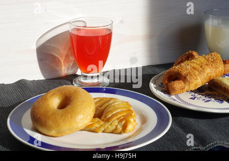 duftendes Frühstück Bagel, Croissant, Bagel, Saft und Milch von der warmen Sonne des Morgens beleuchtet Stockfoto