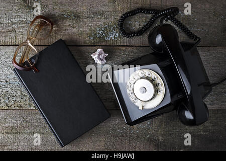 Schwarze Vintage Telefon, alte Gläser und Notebook mit hölzernen Hintergrund Nahaufnahme, Draufsicht, greifen Sie zum Telefon Stockfoto