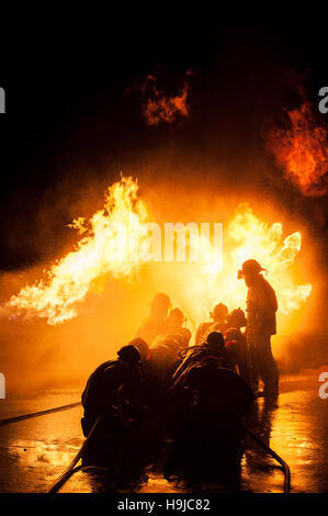 Silhouette der Feuerwehrleute kämpfen ein wütendes Feuer mit riesigen Flammen des brennenden Holzes Stockfoto