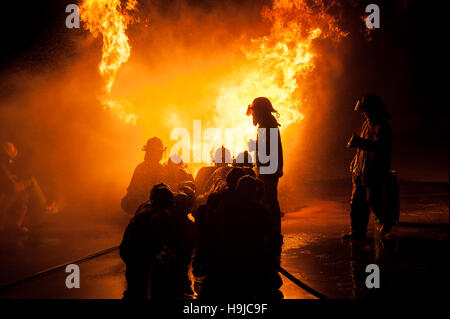 Silhouette der Feuerwehrleute kämpfen ein wütendes Feuer mit riesigen Flammen des brennenden Holzes Stockfoto