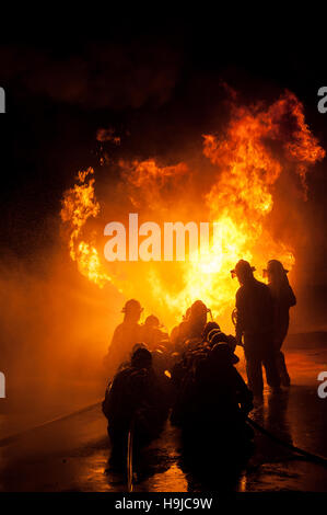 Silhouette der Feuerwehrleute kämpfen ein wütendes Feuer mit riesigen Flammen des brennenden Holzes Stockfoto