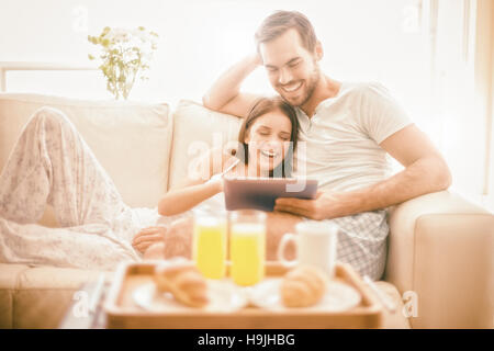 Entspannen Sie sich auf der Couch mit Tablette zum Frühstück nettes Paar Stockfoto