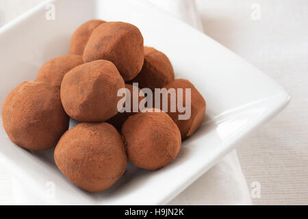Hand gerollt Schokolade Trüffel in Kakao Pulver bestäubt, der mit einem weißen Teller auf eine weiße Tischdecke serviert. Stockfoto