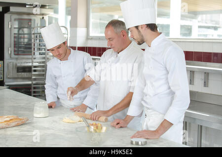 Chefkoch zeigt zwei Auszubildende, wie Teig zubereiten Stockfoto