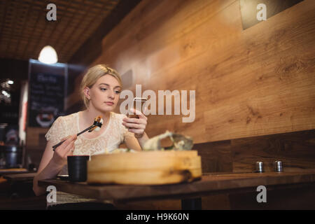 Frau mit Handy beim Sushi-Essen Stockfoto