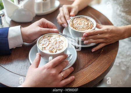 Hände der Braut und des Bräutigams mit Latte Art Kaffee Tasse Stockfoto