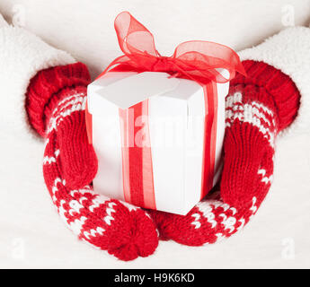 Weibliche Hände halten Weihnachtsgeschenk in rote Handschuhe Stockfoto