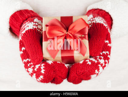 Weibliche Hände halten Weihnachtsgeschenk in rote Handschuhe Stockfoto