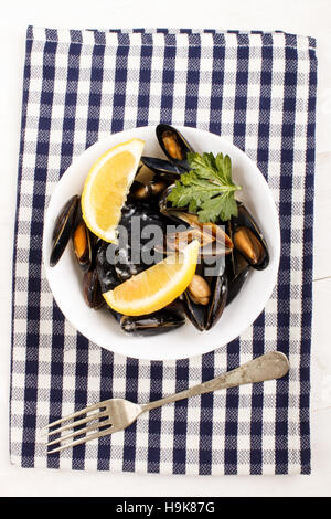 schottische Miesmuscheln in Weißweinsauce, mit Zitrone und Petersilie in einer Schüssel auf einem Küchentuch gekocht Stockfoto