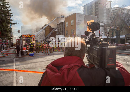 Montreal, CA - 23. November 2016: ein Kameramann filmt Feuerwehrleute arbeiten an Cafe Amusement 68 Gebäude in Brand, 3464 Park Avenue. Stockfoto