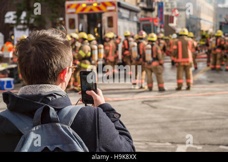 Montreal, Ca - 23. Nov. 2016: männlich Fußgängerzone Bilder nimmt mit Smartphone als Feuerwehrmänner auf 'Cafe Amusement 68' arbeiten Stockfoto