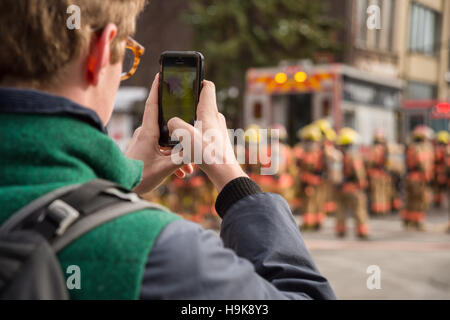 Montreal, Ca - 23. Nov. 2016: männlich Fußgängerzone Bilder nimmt mit Smartphone als Feuerwehrmänner auf 'Cafe Amusement 68' arbeiten Stockfoto