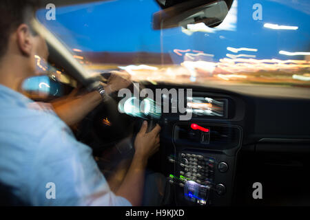 Autofahren in der Nacht - junger Mann mit seinem modernen Auto nachts in einer Stadt (flachen DOF; getönten Farbbild, Unschärfe-Motion-Technik verwendet, um Spe vermitteln Stockfoto