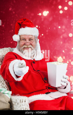 Zusammengesetztes Bild des Weihnachtsmannes mit Popcorn während des Fernsehens Stockfoto