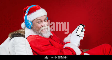 Zusammengesetztes Bild des Weihnachtsmannes mit Kopfhörer mit Handy Stockfoto