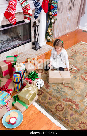 Kleine Mädchen Weihnachtsgeschenke zu Hause sitzen auf dem Boden im Wohnzimmer neben einen Haufen bunte Geschenke und Dekoration Strümpfe Verpacken der Stockfoto