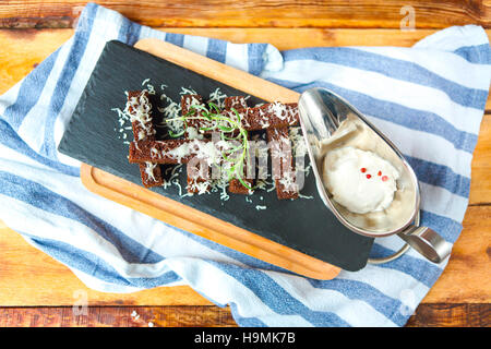 Snack-Braten-Zwieback aus dunklem Brot mit Käse und Knoblauch Sause auf dem Holztisch Stockfoto