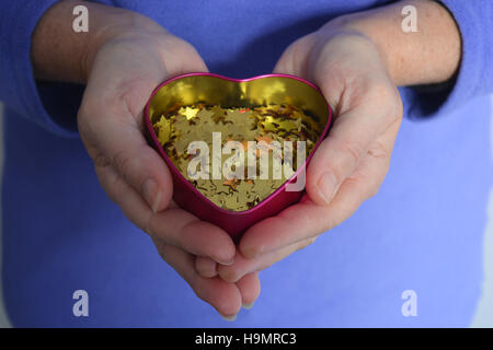 Konzept des Gebens. Frau hält ein Herz gefüllt mit goldenen Sternen. Stockfoto