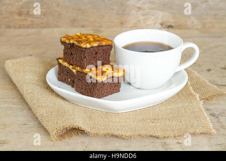 Toffee Kuchen mit Cashew und heißen Kaffee auf Holztisch garnieren. Stockfoto