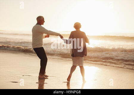 Voller Länge Schuss älteres Paar, die Spaß am Strand bei Sonnenuntergang. Älteres Paar gemeinsam Urlaub im Sea Shore. Stockfoto