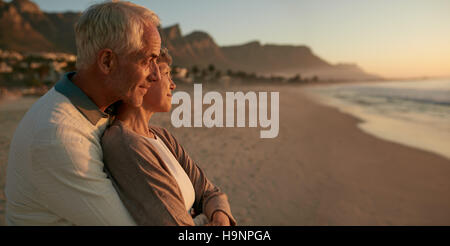 Richtungskontrolle Ansicht der senior Liebespaar am Strand den Sonnenuntergang genießen. Älteres paar zusammenstehen und umarmt am Ufer Meeres. Stockfoto