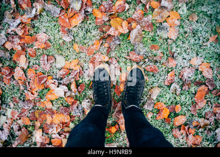 Teenager Beine in Leder Stiefel stehen auf Boden mit Laub bedeckt mit Schnee, Ansicht von oben. Saison-Änderung-Konzept Stockfoto