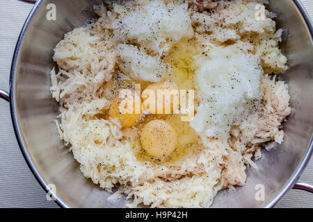 Geriebene Kartoffel und Zwiebel und drei Eiern mit Würze für Latkes in Metall-Behälter von oben Stockfoto
