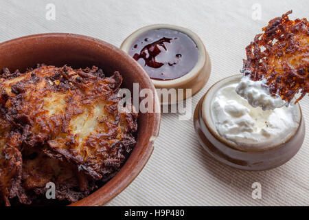 Latkes in eine keramische rustikale braune Schale mit saurer Sahne und Erdbeermarmelade beiseite Latkes mit saurer Sahne drauf von Seite Stockfoto