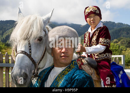 Kasachische Vater und Sohn auf seinem Pferd in traditionellen Kleidern bei der kasachischen Schau der Nationalspiele in Almaty, Kasachstan Stockfoto