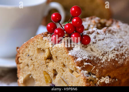 Nahaufnahme eines Stückes Früchtekuchen für die Weihnachtszeit bestreut mit Puderzucker neben einer weißen Keramik Tasse mit Kaffee oder Tee Stockfoto