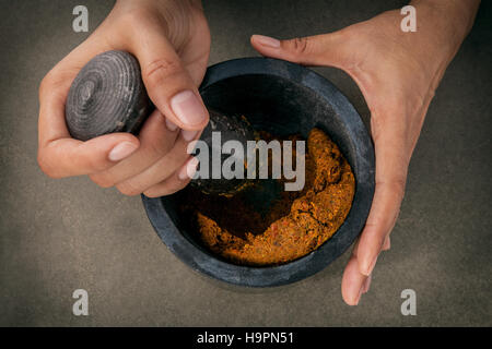 Die Frauen halten Stößel mit Mörtel und und rote Currypaste würzen Stockfoto