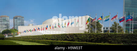 UN-Generalversammlung mit Weltflaggen, die an einem sonnigen Tag mit blauem Himmel vor sich fliegen - First Avenue, New York City, NY, USA Stockfoto