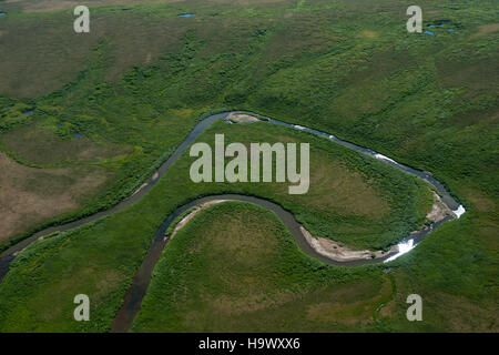Ein ruhiges Foto eines sich schlängelnden Baches in Alaska, das die ruhige Schönheit der Natur mit seinem gewundenen Wasser und der umliegenden Landschaft einfängt. Das Bild zeigt die weite Wildnis des alaskischen Geländes. Stockfoto