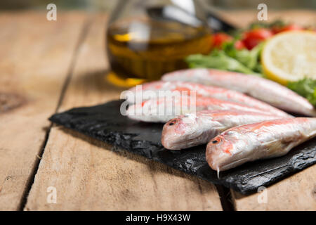Rohe rote Meerbarbe auf geschweiften Salat auf Schiefer Teller auf Holztisch serviert Stockfoto