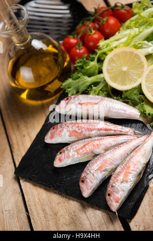 Rohe rote Meerbarbe auf geschweiften Salat auf Schiefer Teller auf Holztisch serviert Stockfoto