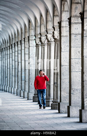 Mann im roten Pullover, spricht auf Handy, zu Fuß durch Säulen und Bögen, Plaza de Armas, Arequipa, Peru Stockfoto